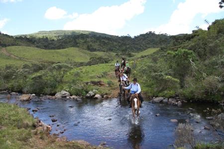 Riding group crossing a river in the green hills of Santa Catarina, Brazil