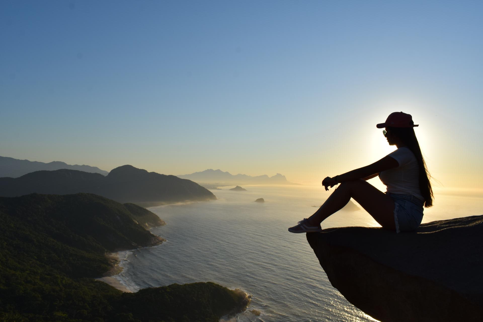 Woman sitting at sunrise on Pedra do Telégrafo overlooking Rio de Janeiro’s coastline