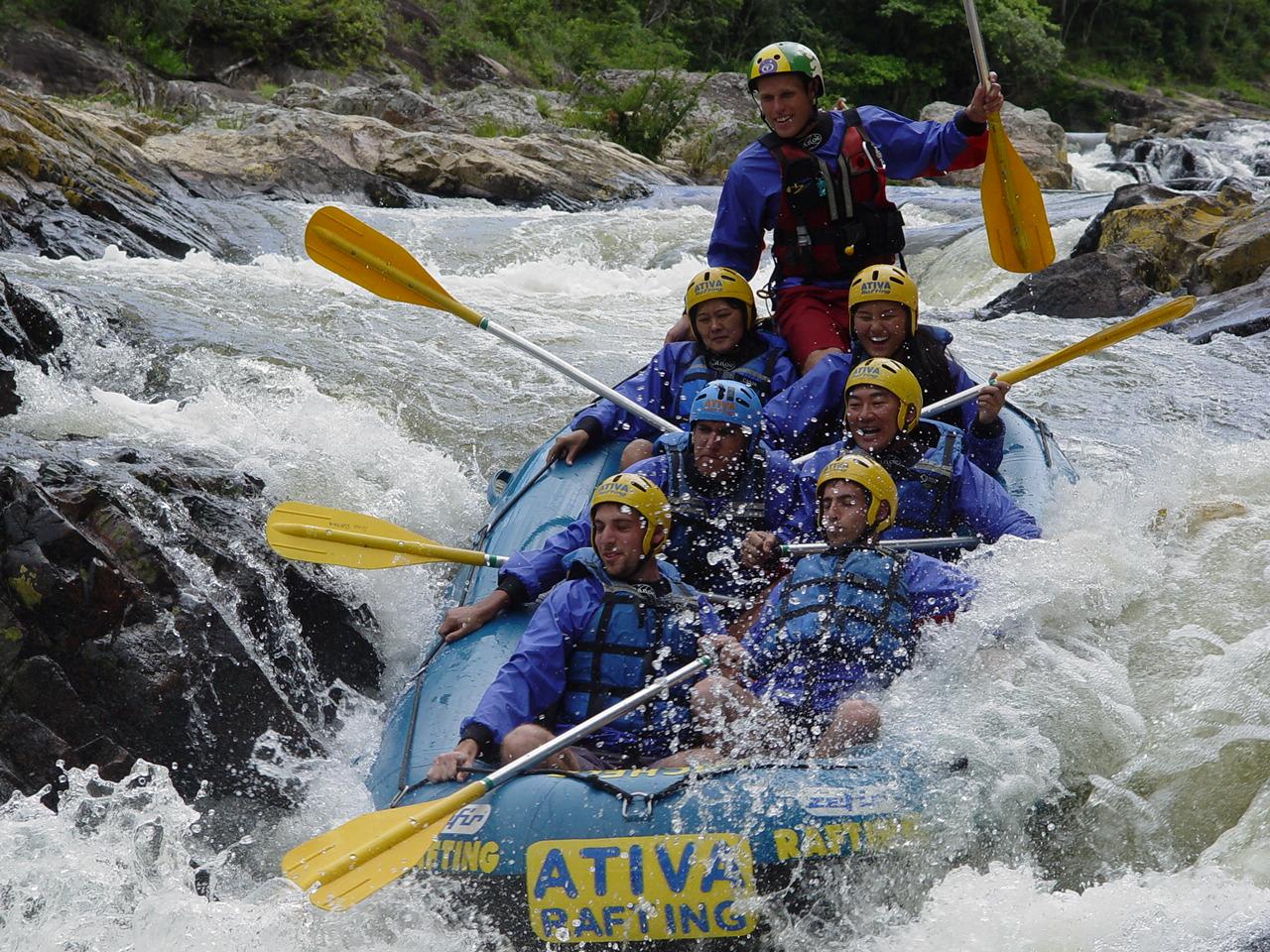 Group whitewater rafting in Brazil in an inflatable boat with helmets and paddles, surrounded by splashing water and rocks