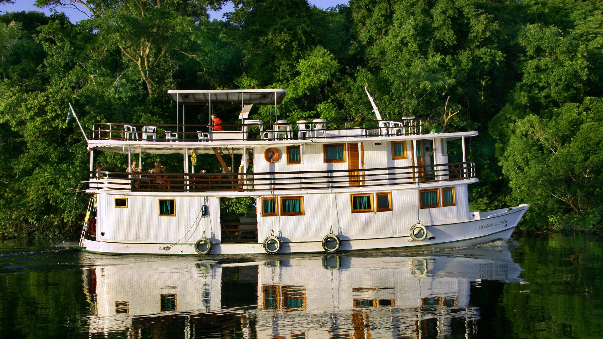 A white Amazon Clipper Boat reflecting on the dark waters of a Amazon riverarm