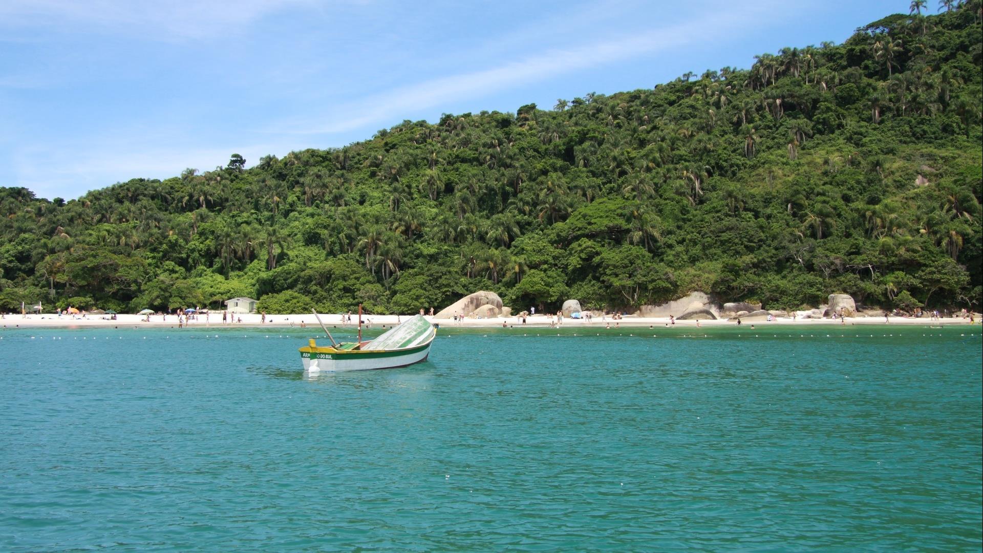 A boat on the green sea and in front of a lonly beach, surounded by Atlantic Rainforest